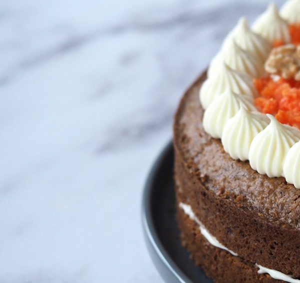 Foto de una tarta de zanahoria o carrot cake con decoración de queso crema y zanahoria confitada